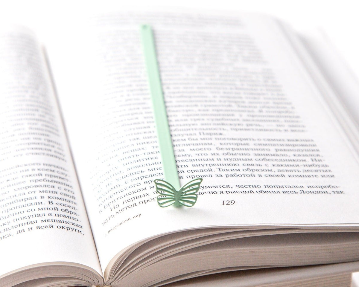 Mint Butterfly metal bookmark in green resting on the pages of an open book
