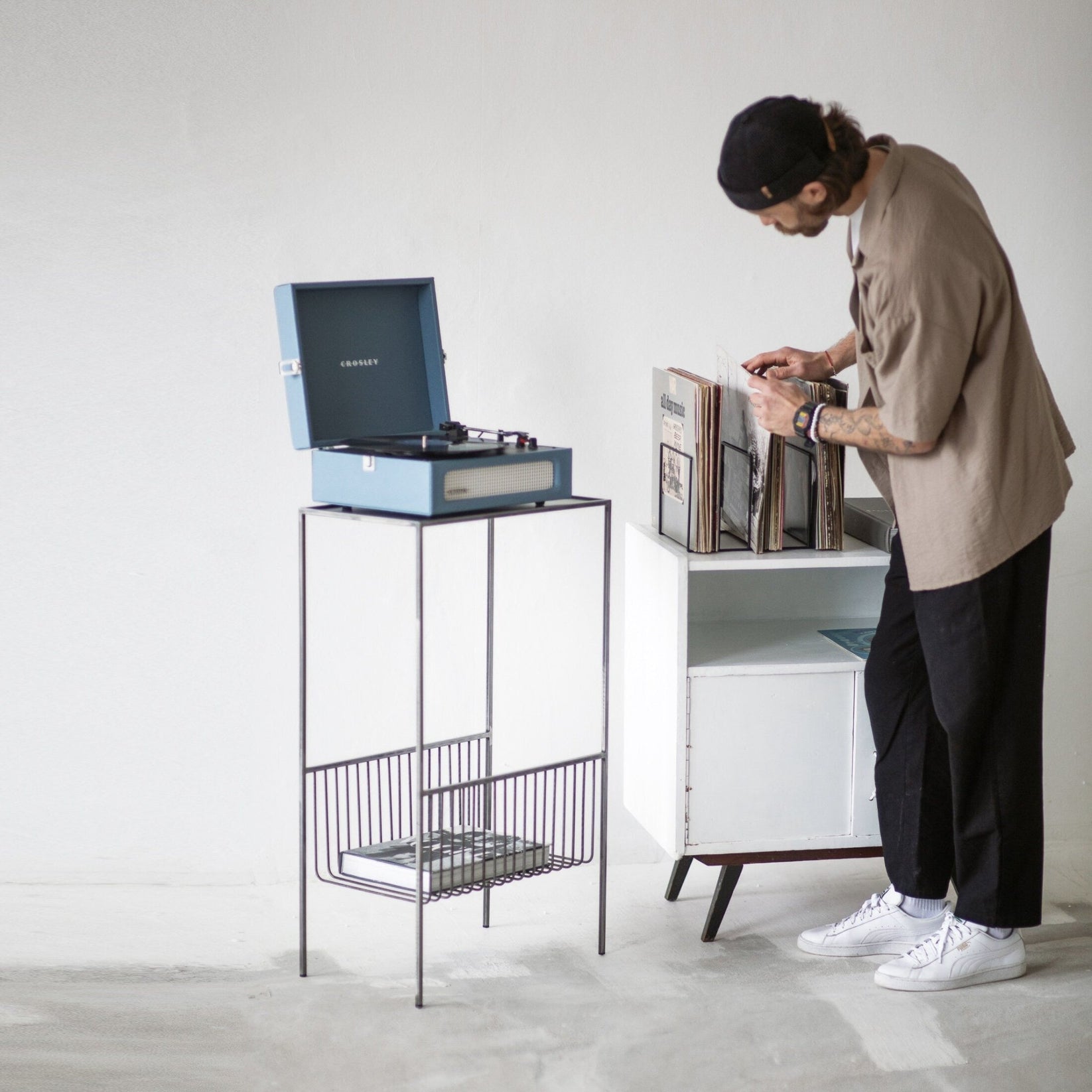 Person browsing vinyl beside the record player stand with an empty lower basket