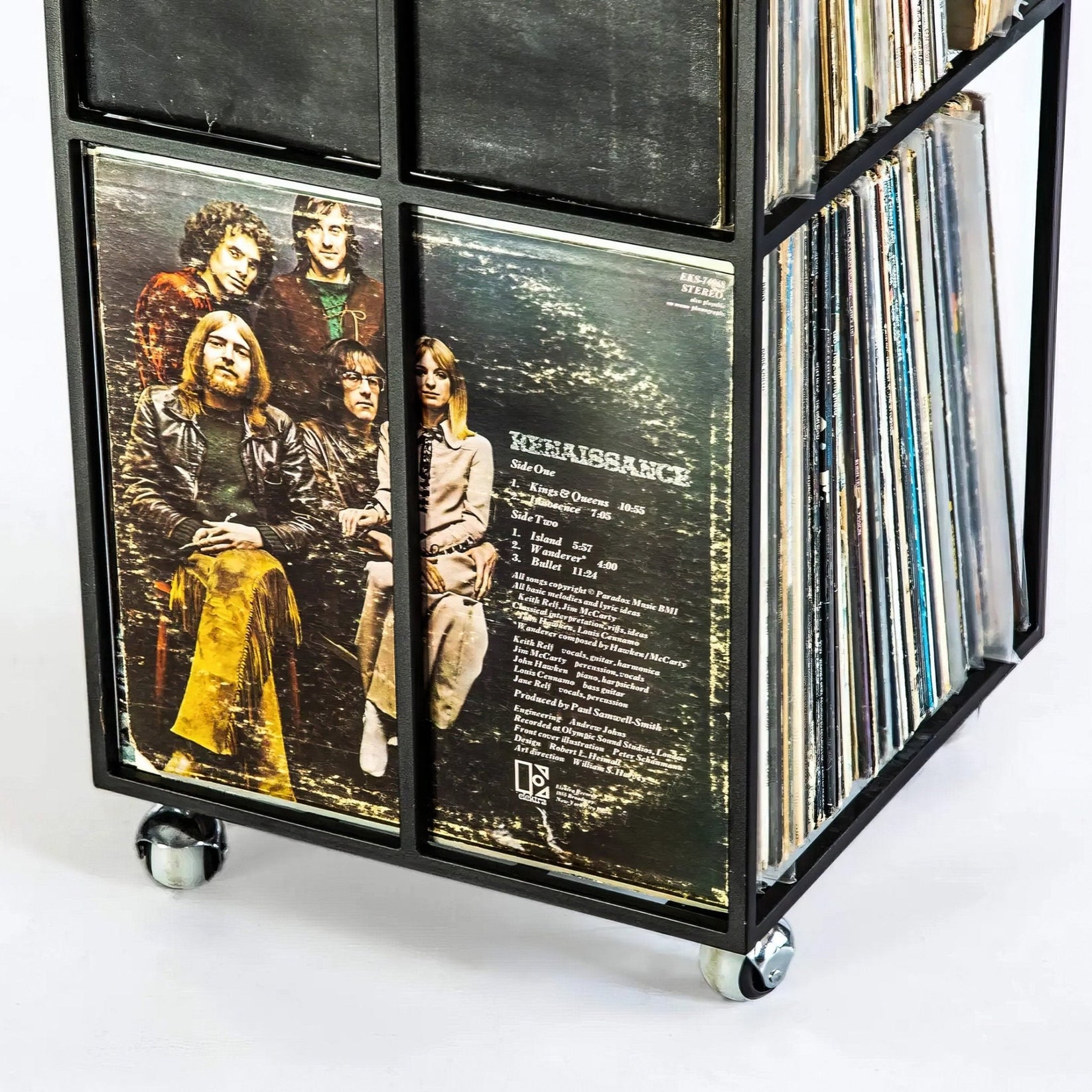Close-up of black metal vinyl record holder on wheels, featuring a Renaissance LP with visible band members and song list, packed with vintage records.