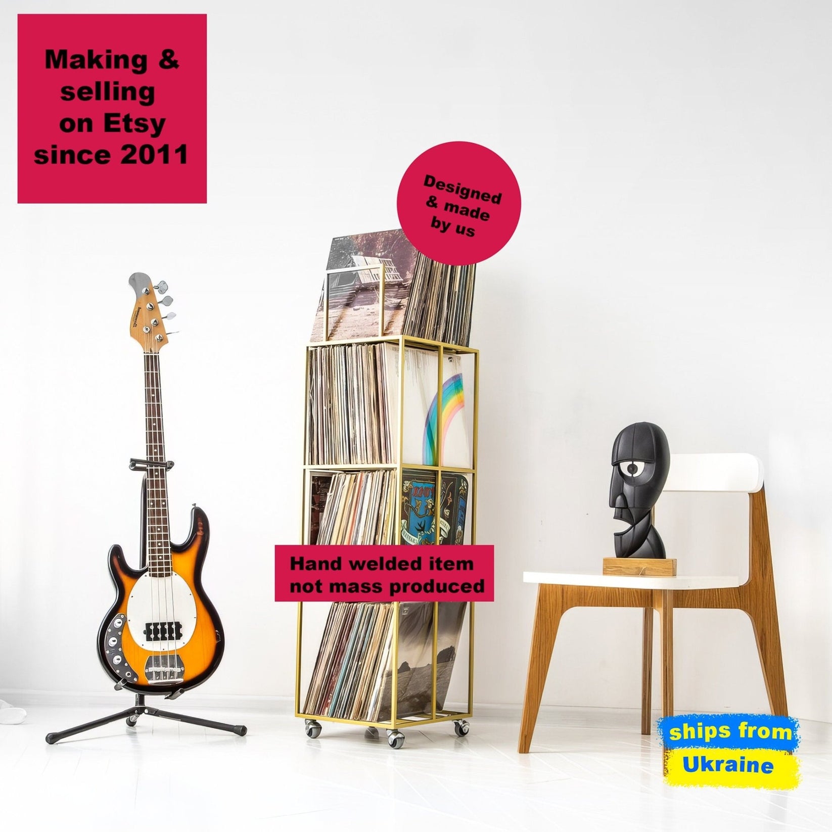 Tall gold metal vinyl record rack on wheels, with four compartments, filled with LPs. Displayed in a modern room with a bass guitar and designer chair.