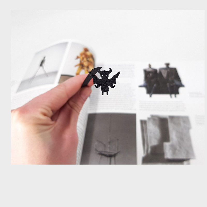 Monster Chupacabra metal bookmark held in a hand above an open book