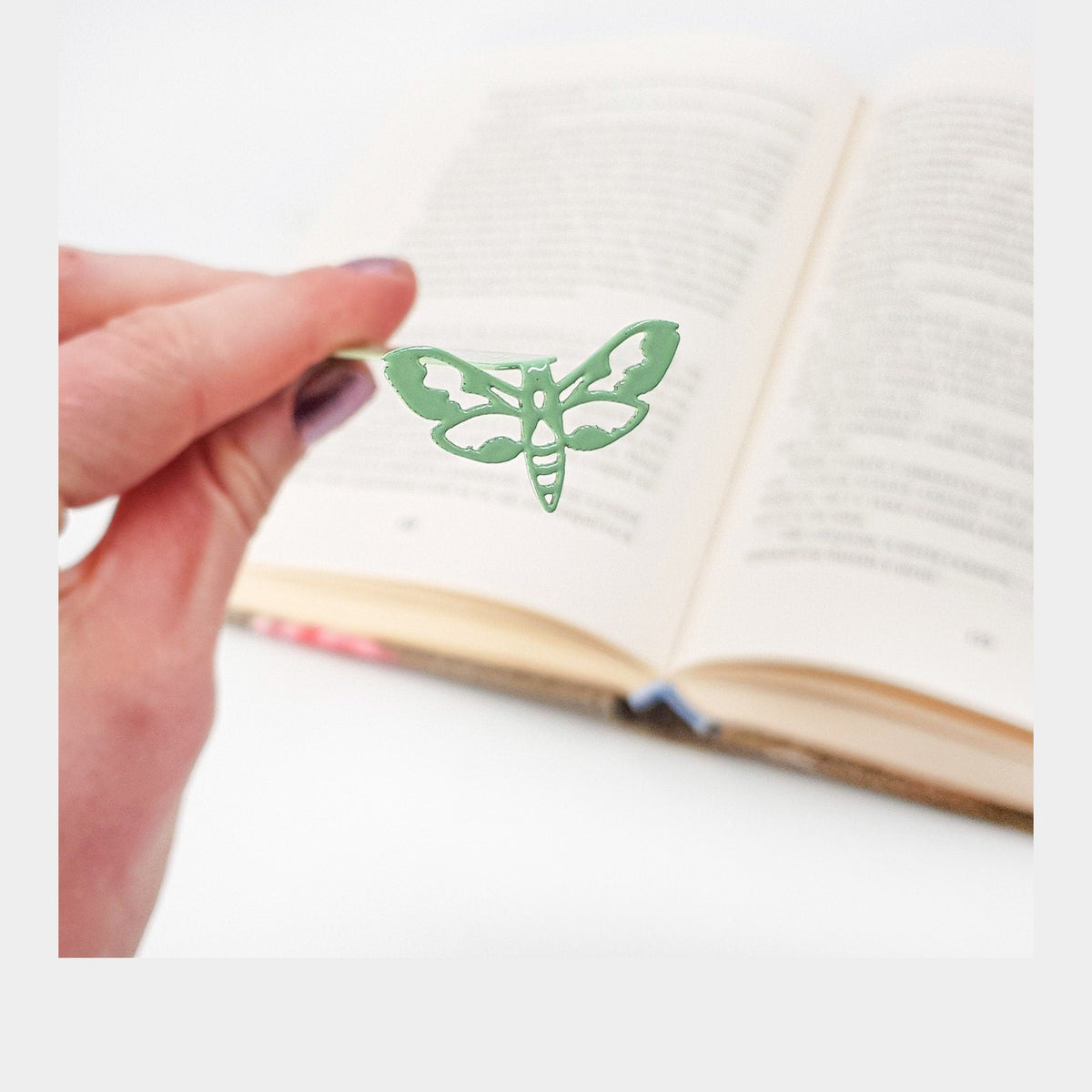 Moth metal bookmark in green held in a hand above an open book