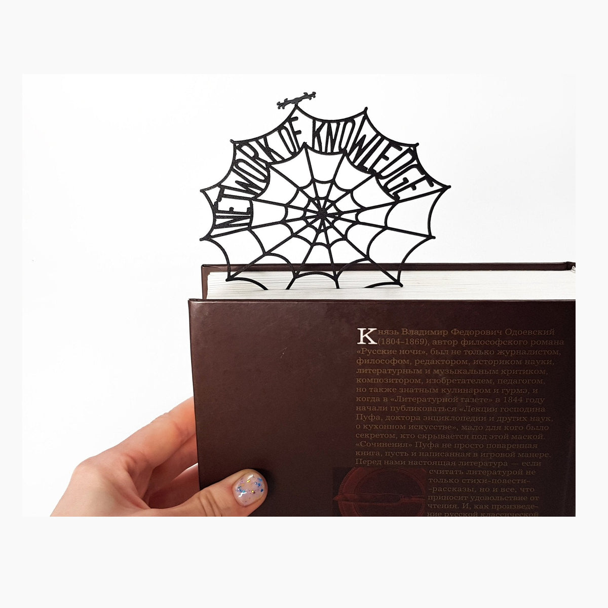 Network of Knowledge metal bookmark held in a hand above an open book