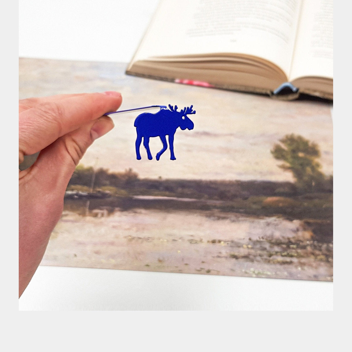 Norwegian Moose metal bookmark in blue marking a page in an illustrated book