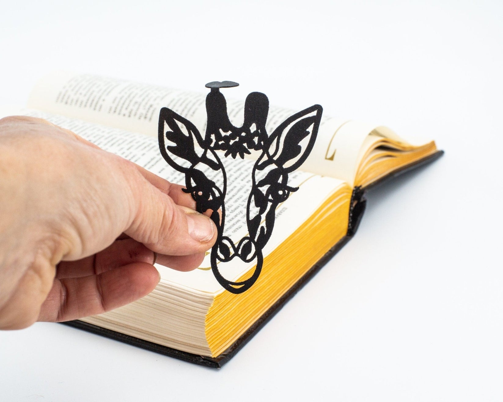 Giraffe Head metal bookmark held in a hand above an open book
