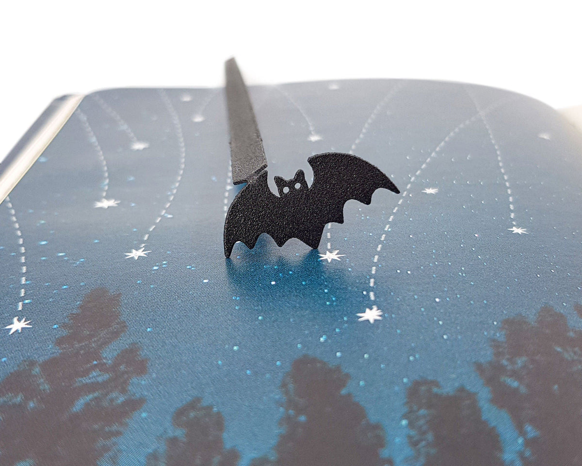 Kitti Bat metal bookmark marking a page in an illustrated book
