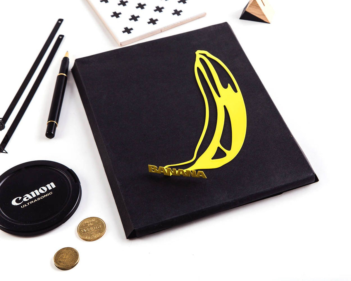 One Banana metal bookmark in gold marking a page in a notebook