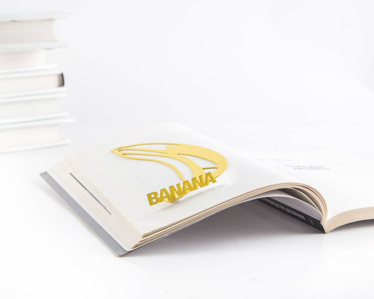 One Banana metal bookmark in gold marking a page in an open book