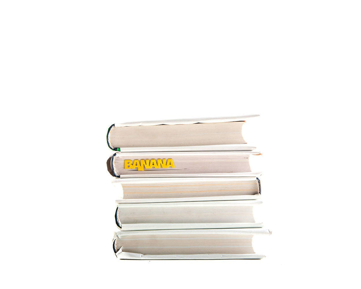 One Banana metal bookmark in gold shown with a stack of books