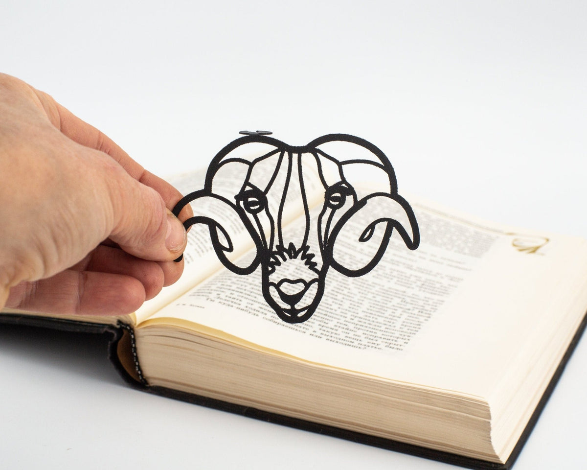 Ram's Head metal bookmark held in a hand above an open book
