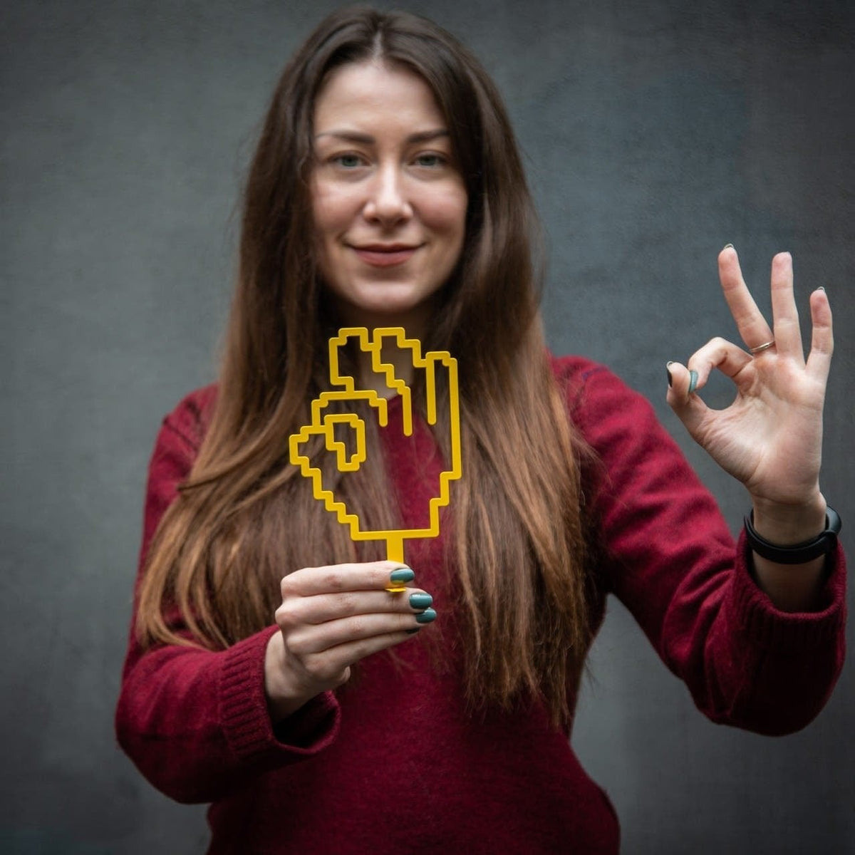 OK Sign Pixel Style metal bookmark in gold held in a hand above an open book
