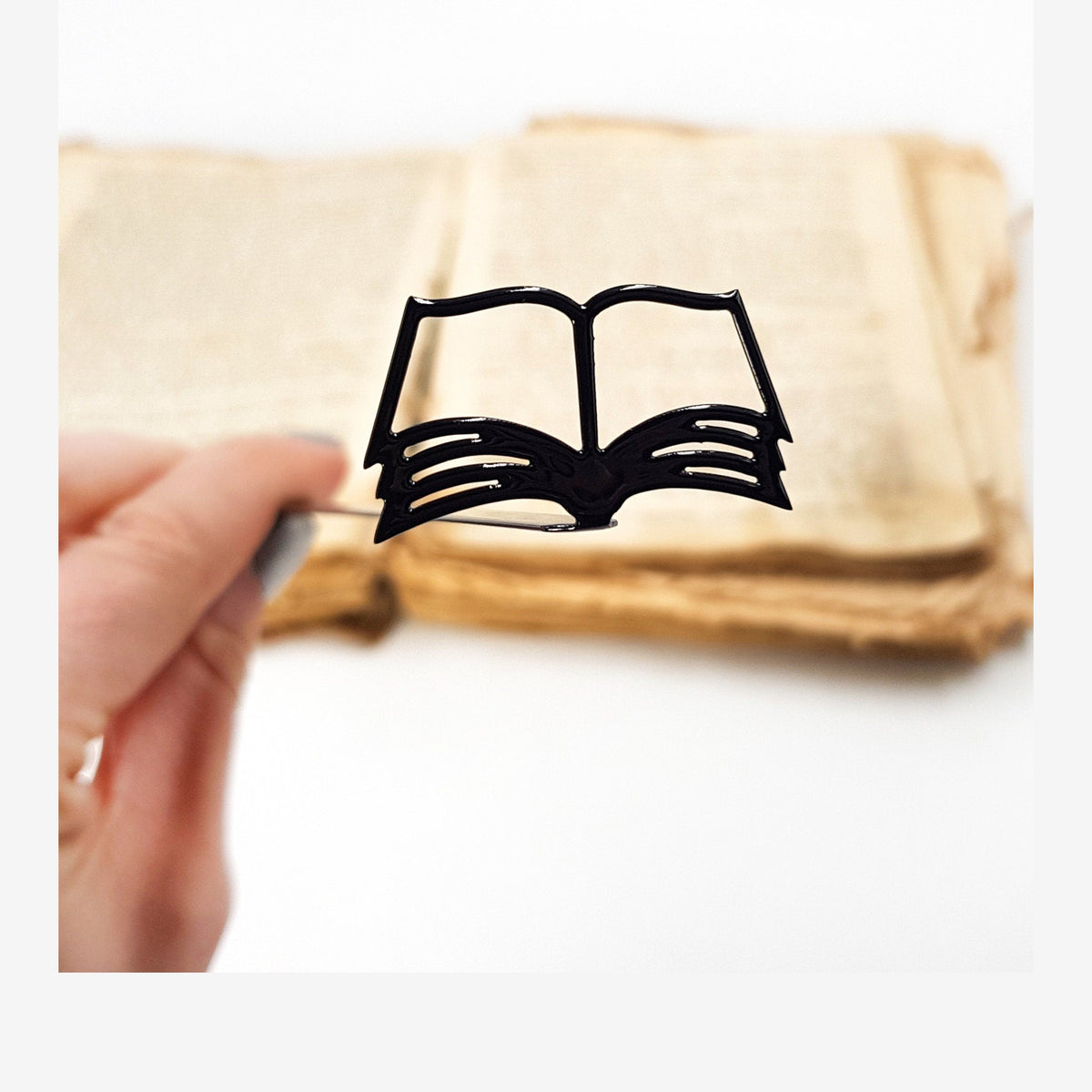 Open Book metal bookmark held in a hand above an open book