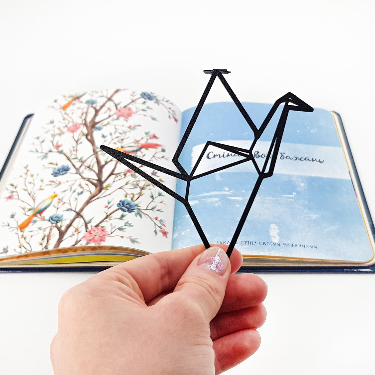 Origami Crane metal bookmark held in a hand above an open book