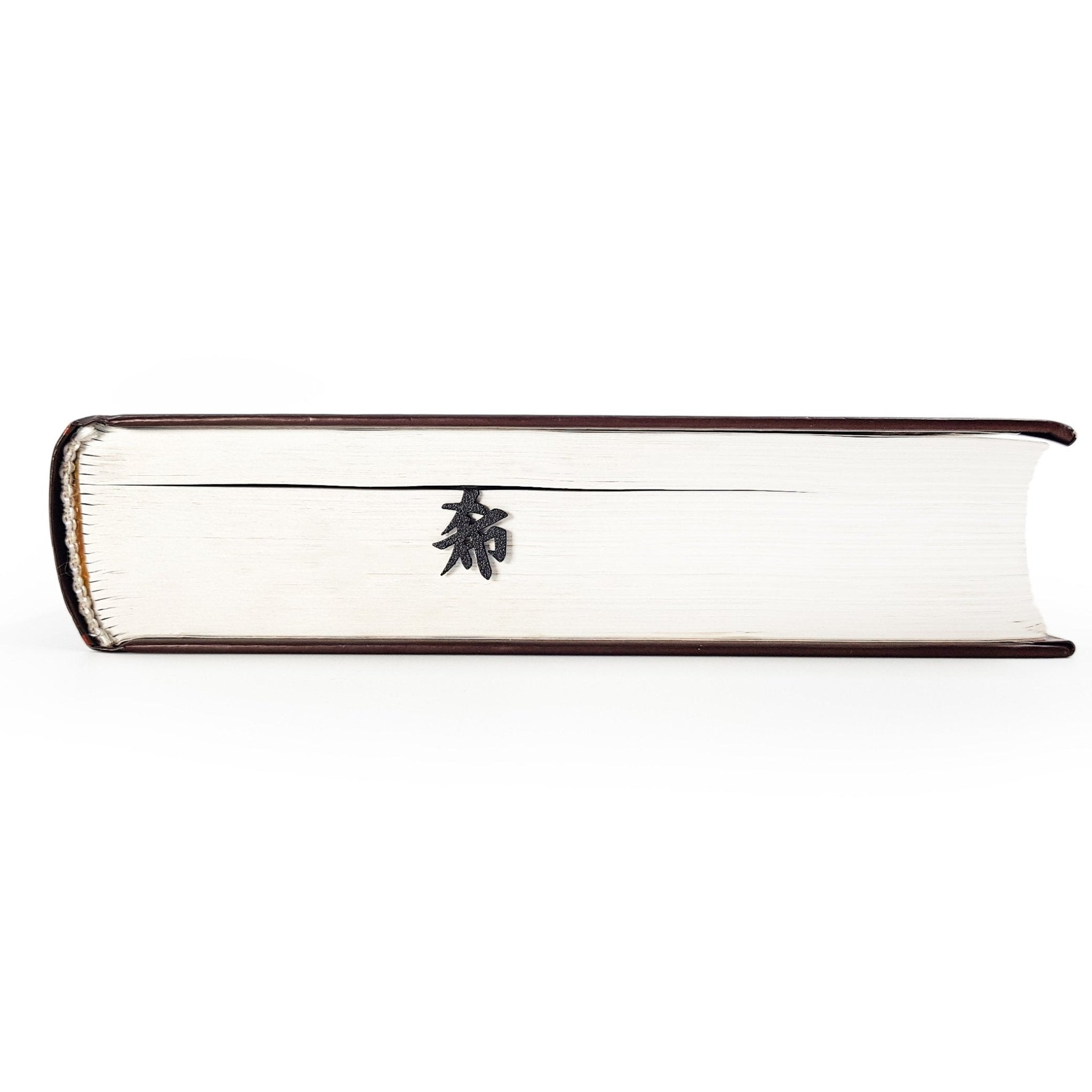 Black metal bookmark with a Zen kanji symbol visible along the page edges of a closed book.