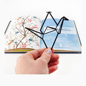 Origami Crane metal bookmark held in a hand above an open book