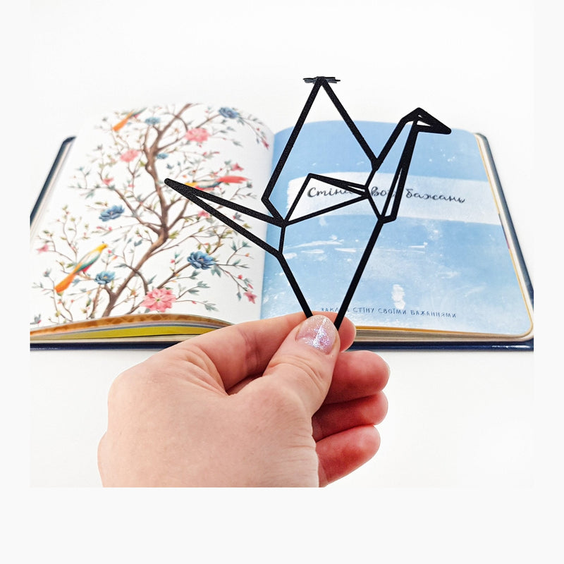 Origami Crane metal bookmark held in a hand above an open book