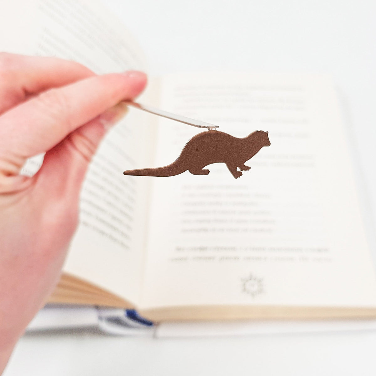 Otter bookmark held in a hand above an open book