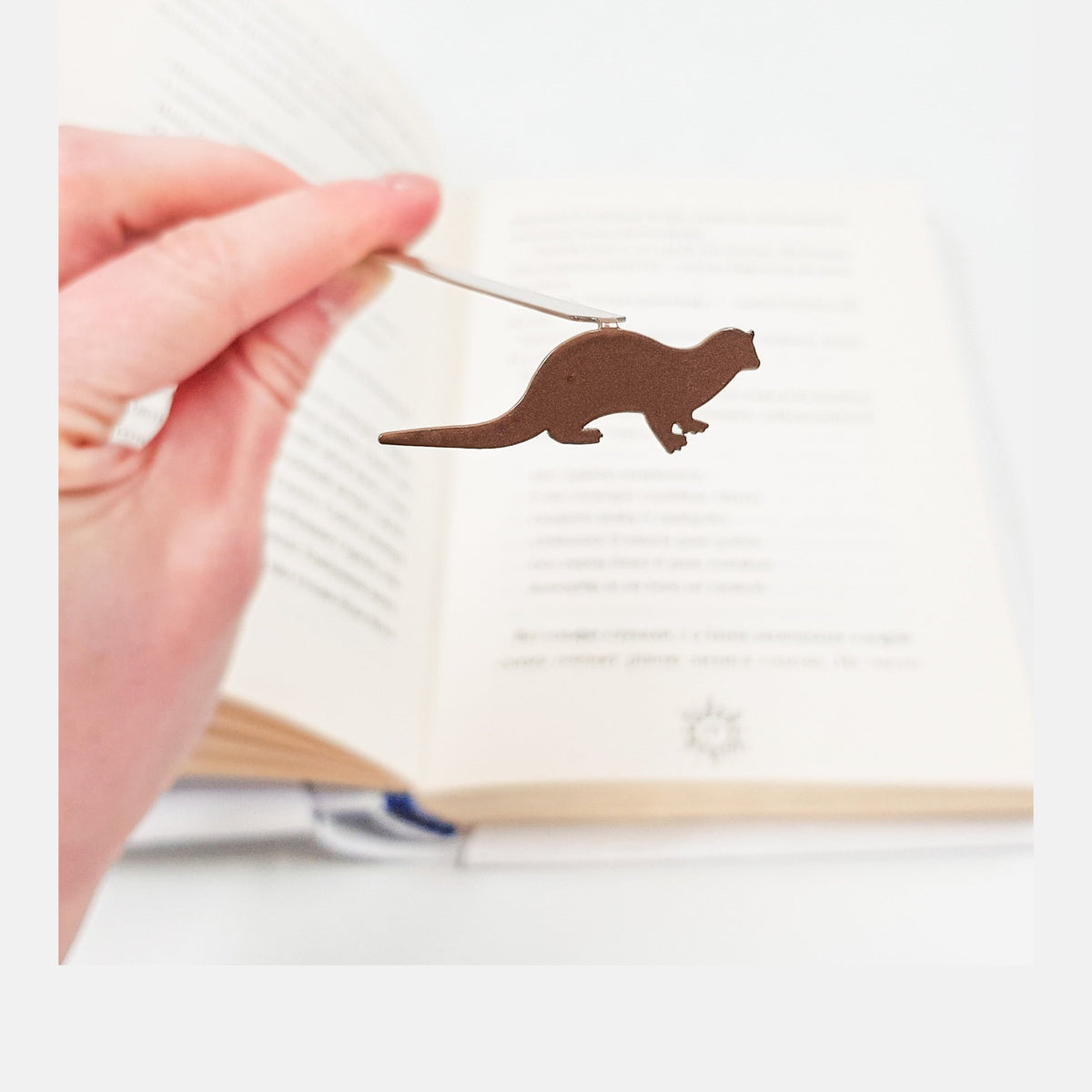 Otter bookmark held in a hand above an open book