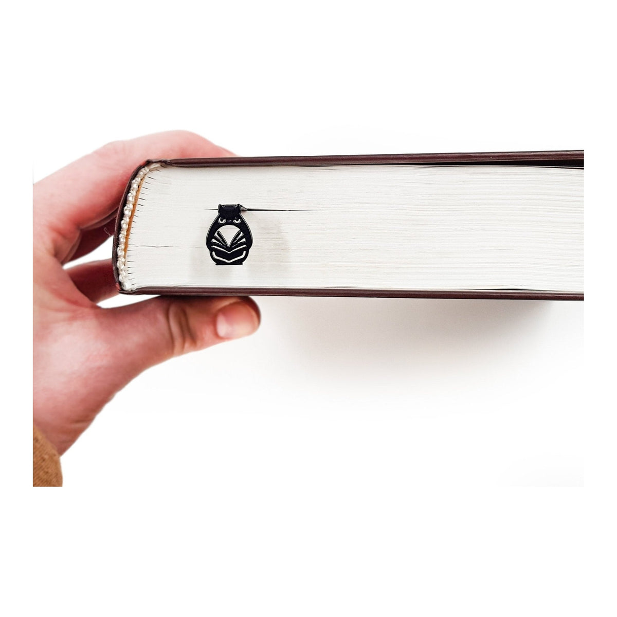 Laser Cut Metal Owl bookmark held in a hand above an open book