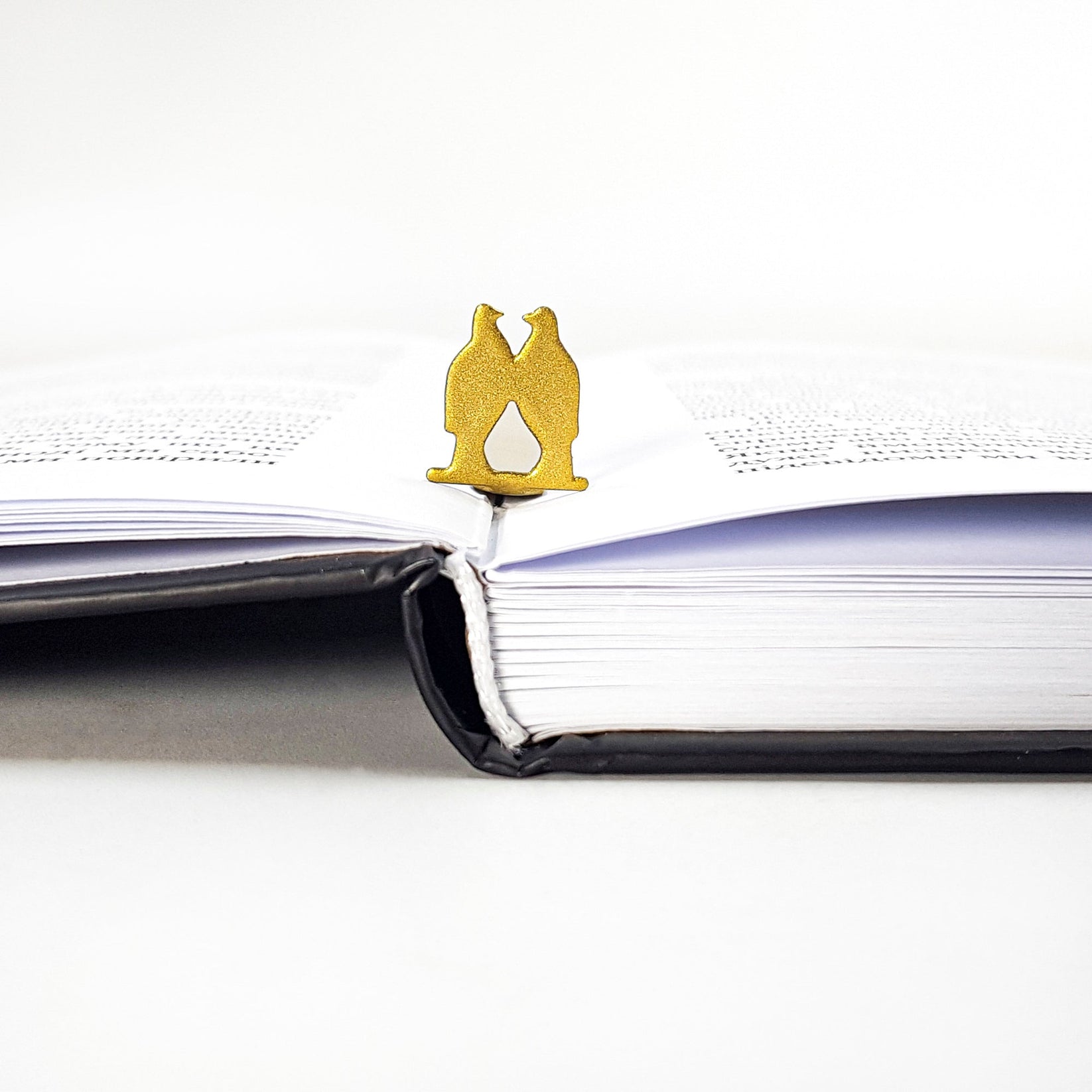 Pair of Pigeons metal bookmark in gold resting on the pages of an open book