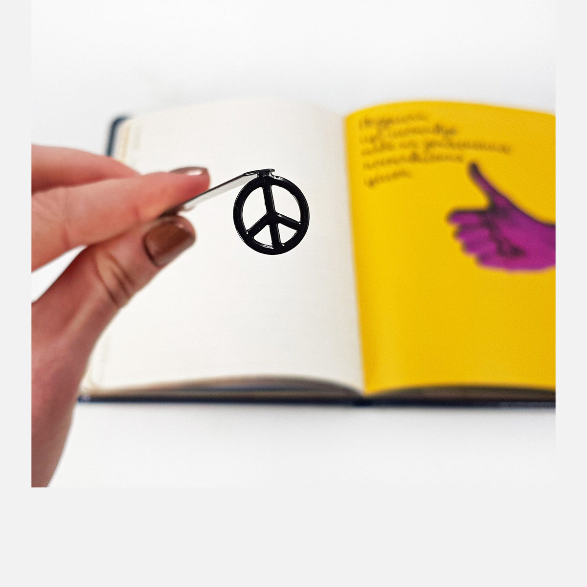 Peace metal bookmark held in a hand above an open book