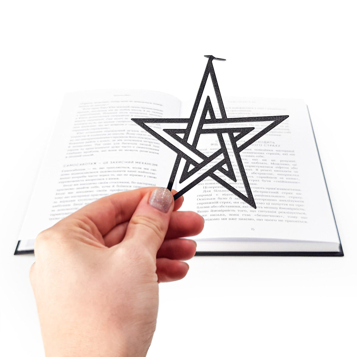 Pentagram & Skull metal bookmark held in a hand above an open book