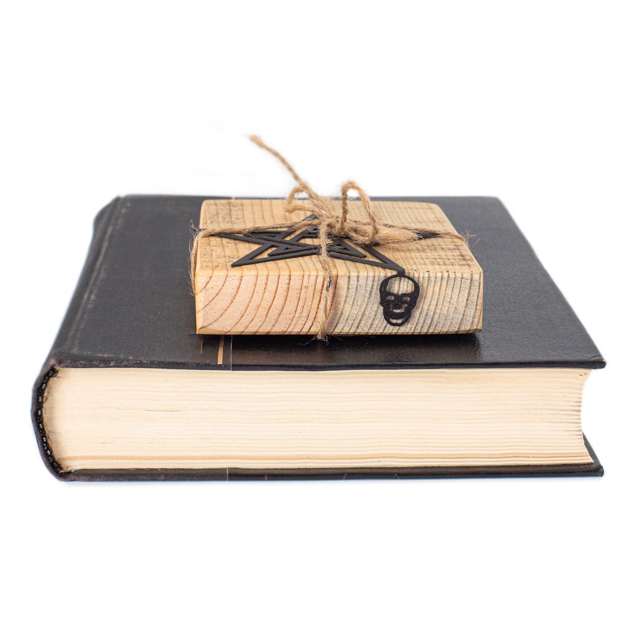 Black metal pentagram and skull bookmark wrapped in wood and jute string, resting on a closed vintage book — handmade gothic page marker.