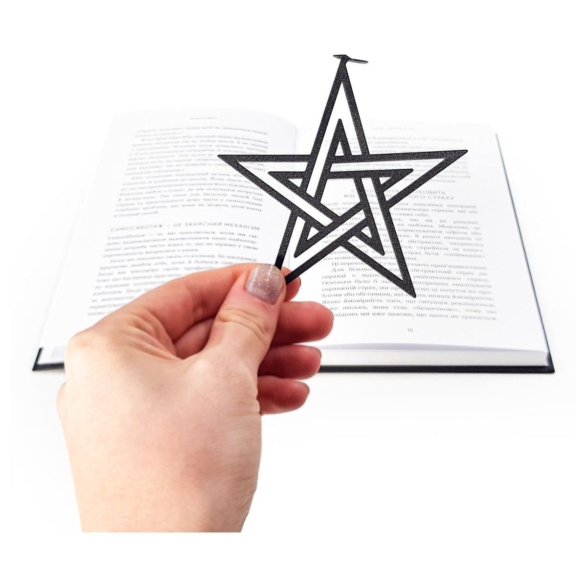 Pentagram & Skull metal bookmark held in a hand above an open book