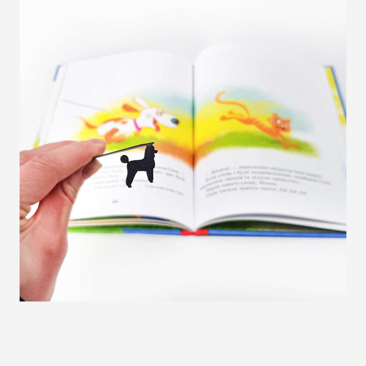 Poodle metal bookmark marking a page in an illustrated book