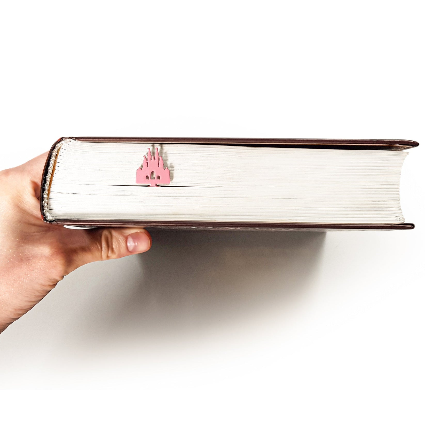 Princess Castle Pink metal bookmark in red held in a hand above an open book
