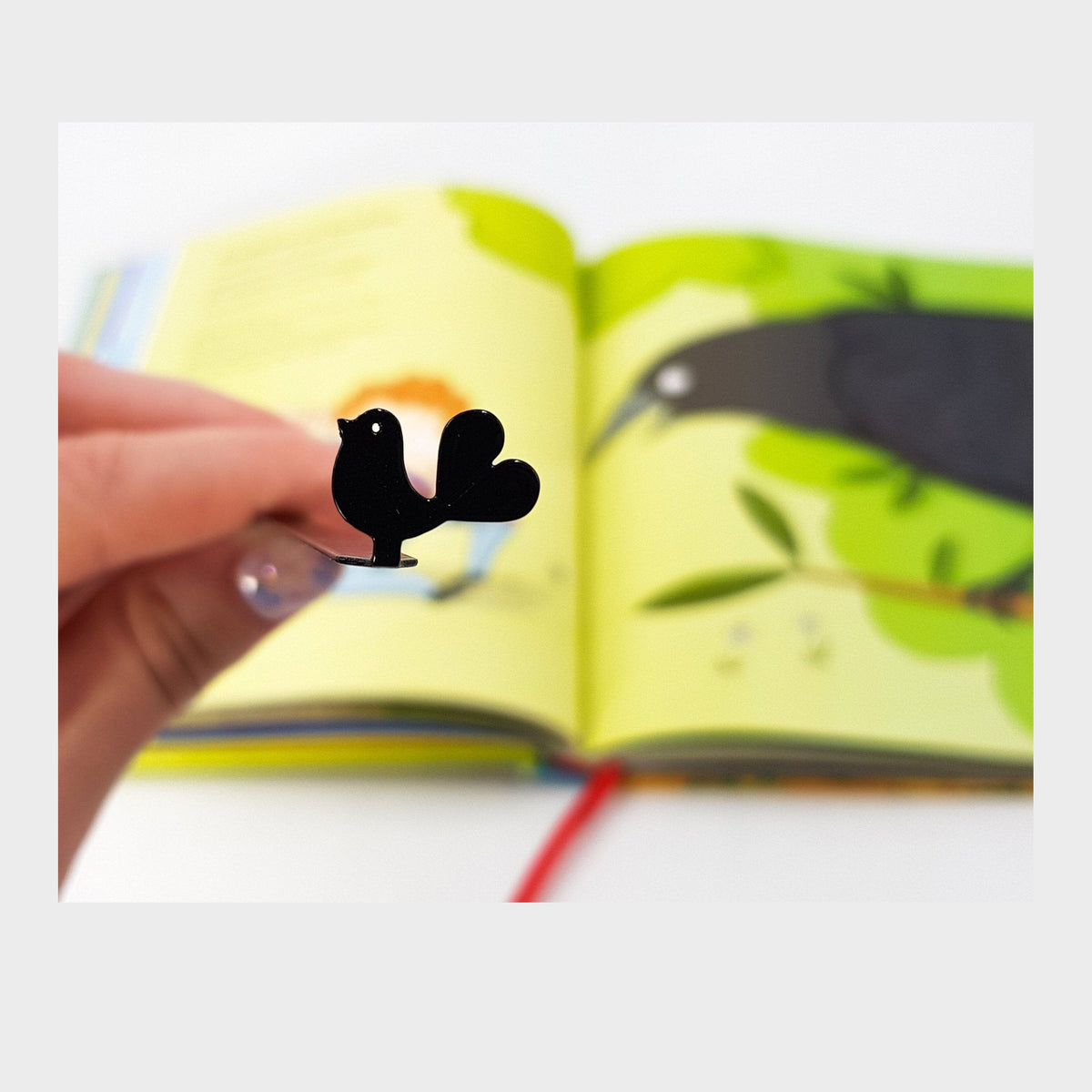 Proud Bird metal bookmark marking a page in an illustrated book