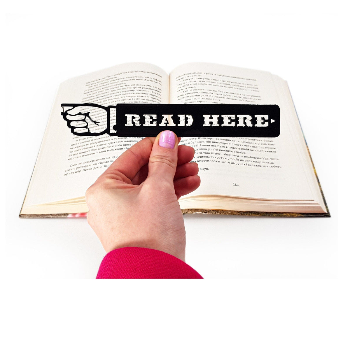 Read Here metal bookmark held in a hand above an open book