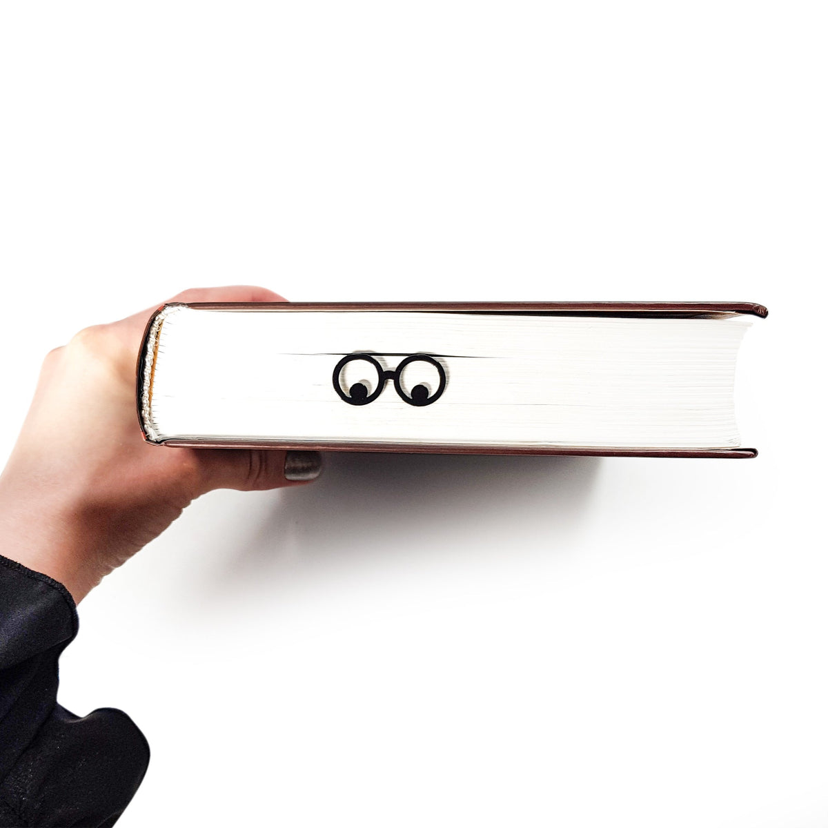 Reading Eyes metal bookmark held in a hand above an open book
