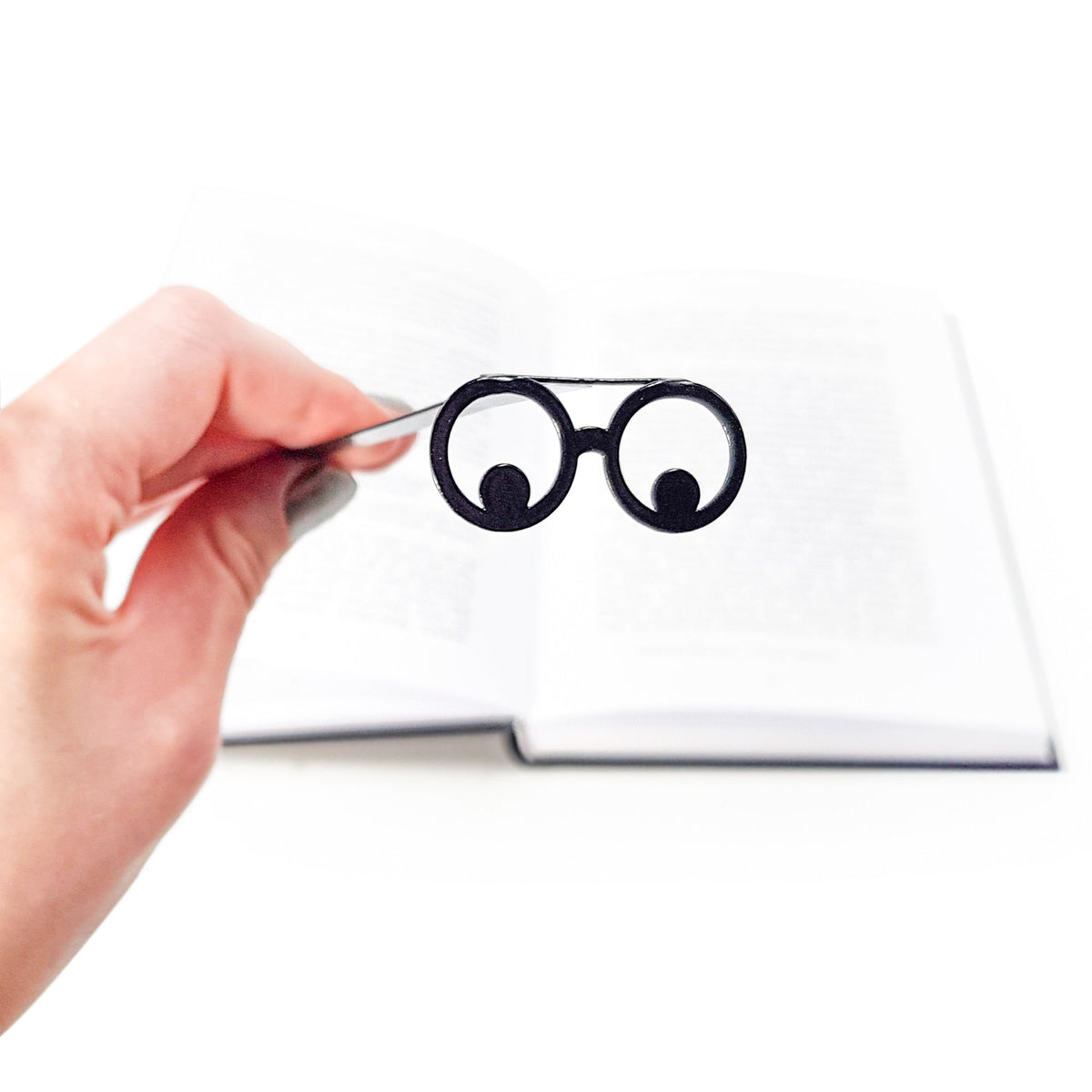 Reading Eyes metal bookmark held up beside an open book
