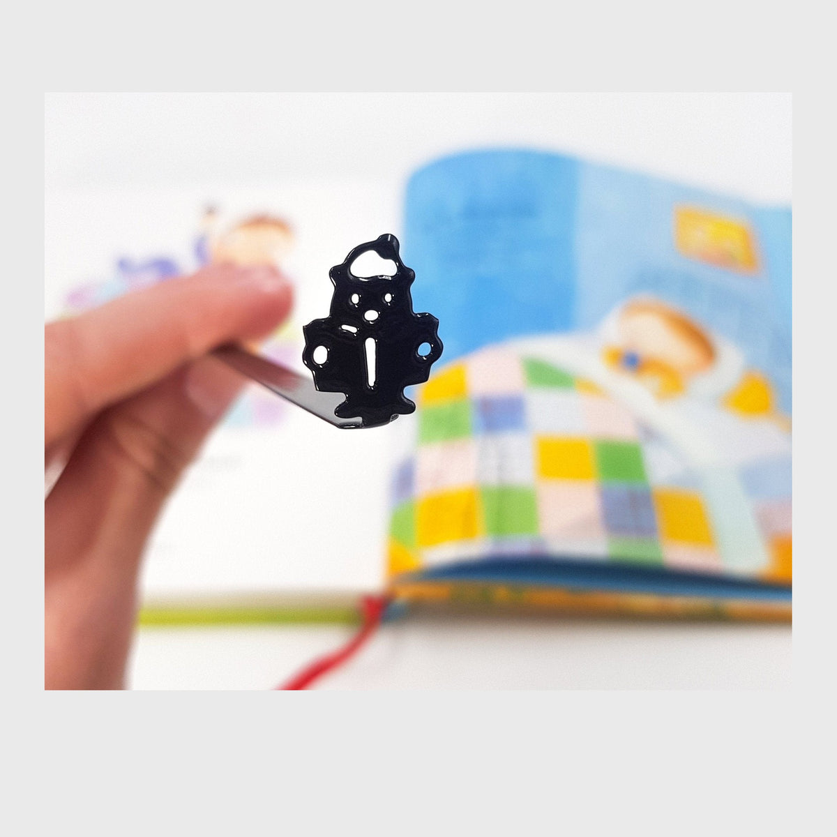 Reading Teddy Bear metal bookmark held in a hand above an open book