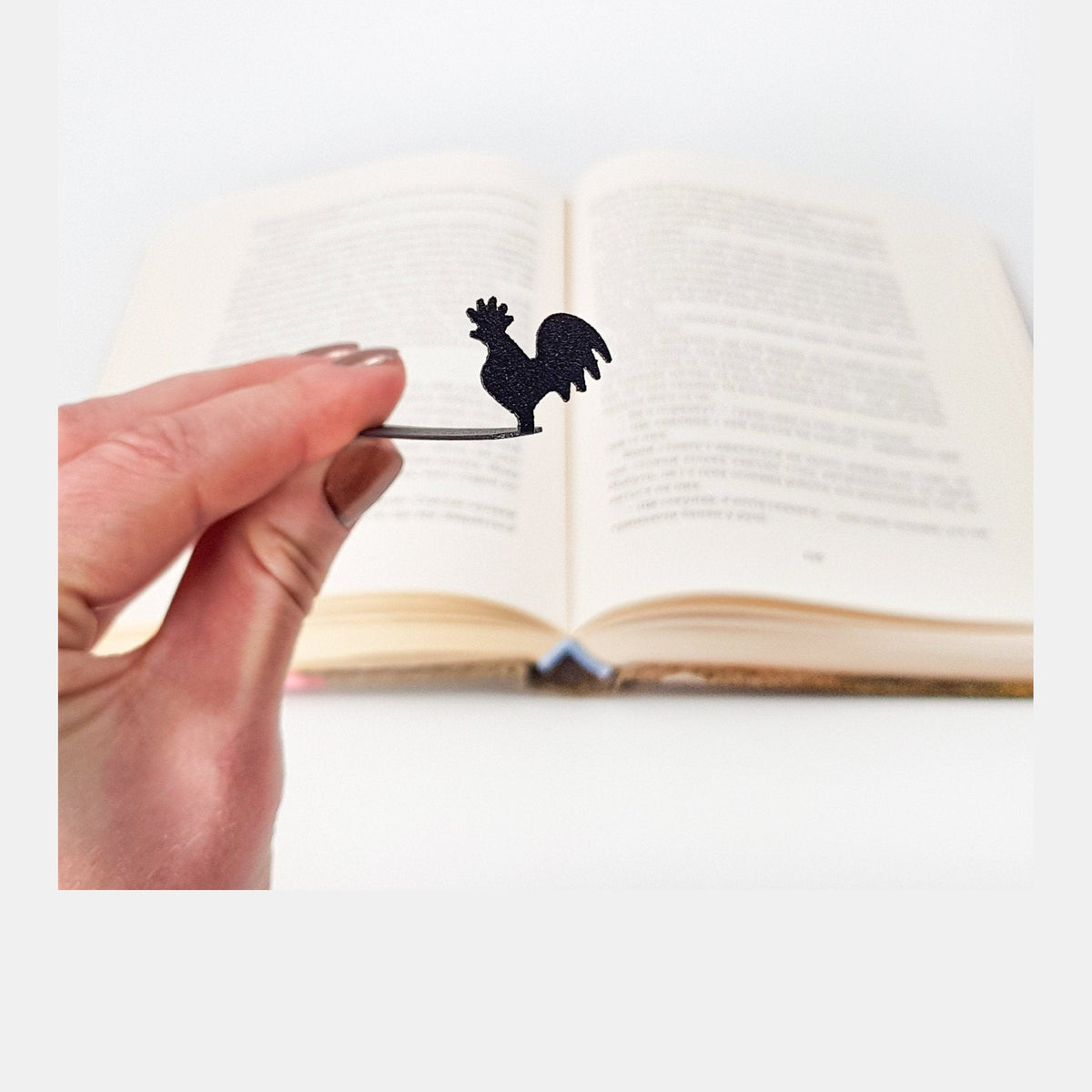 Rooster metal bookmark held in a hand above an open book