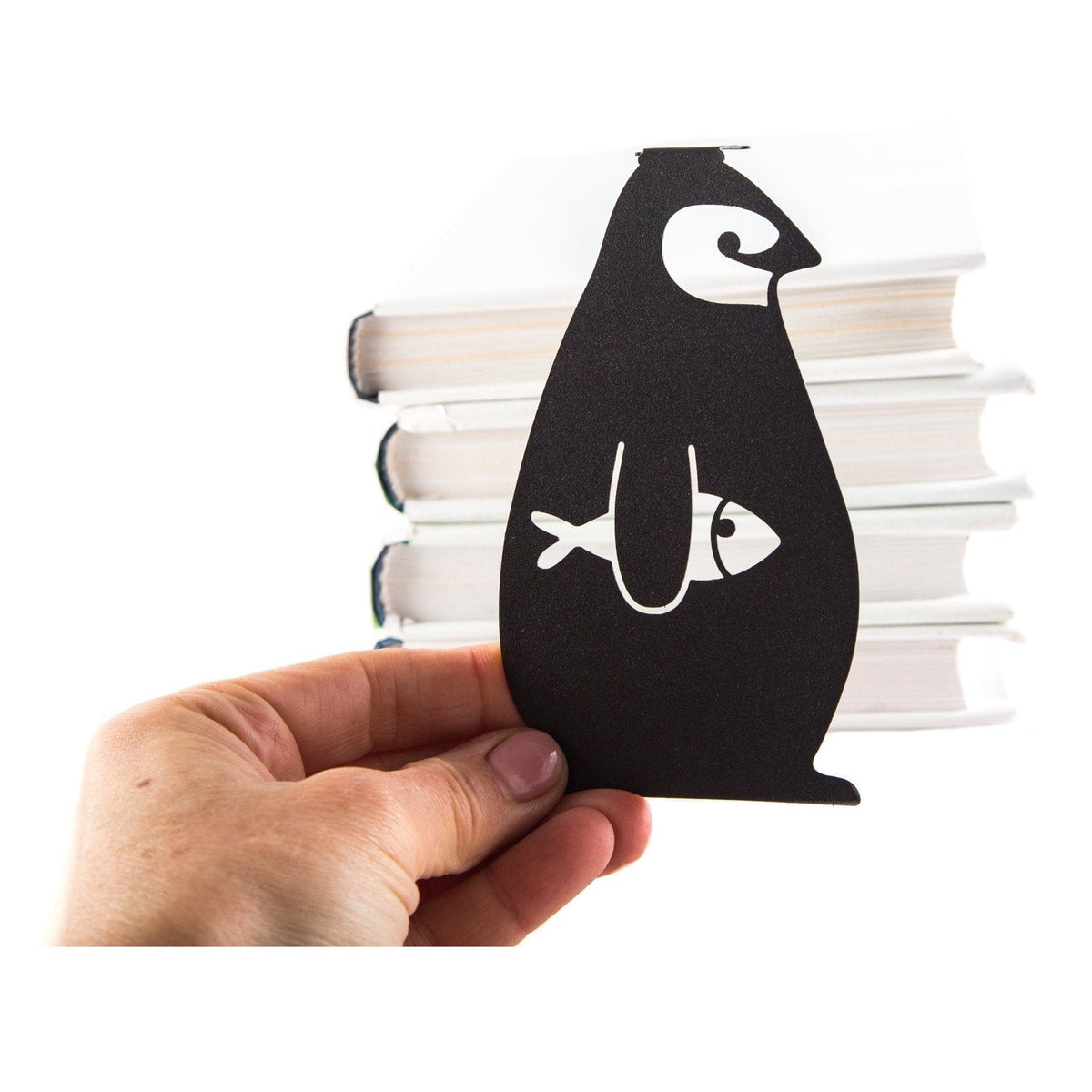 Royal Penguin metal bookmark held in a hand above an open book