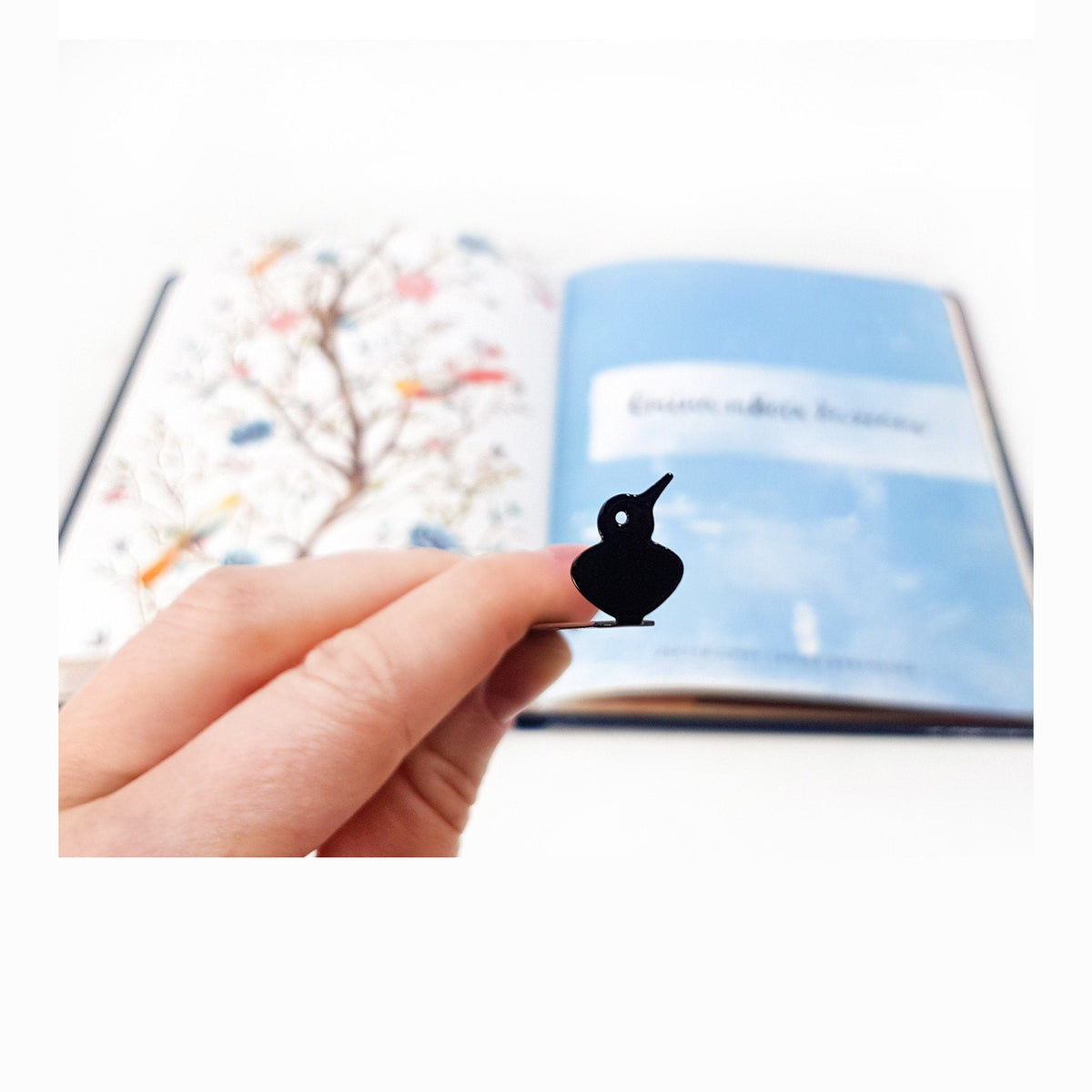 Scandinavian Bird metal bookmark marking a page in an illustrated book