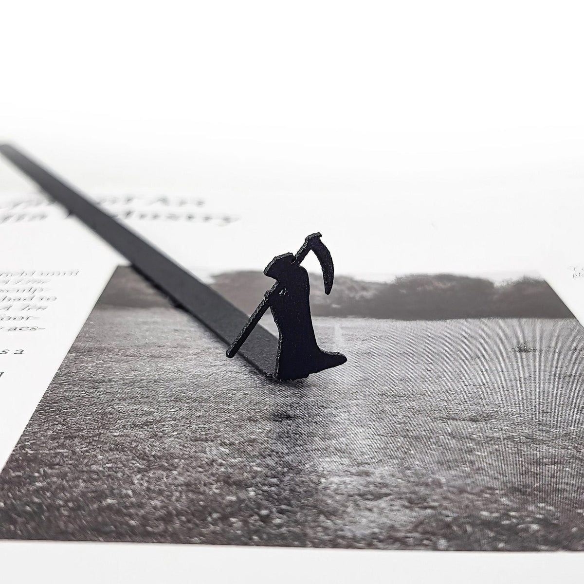 Grim Reaper metal bookmark on an illustrated page