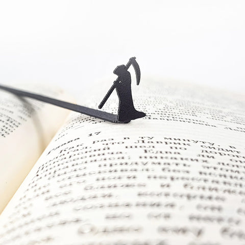 Grim Reaper metal bookmark resting on the pages of an open book