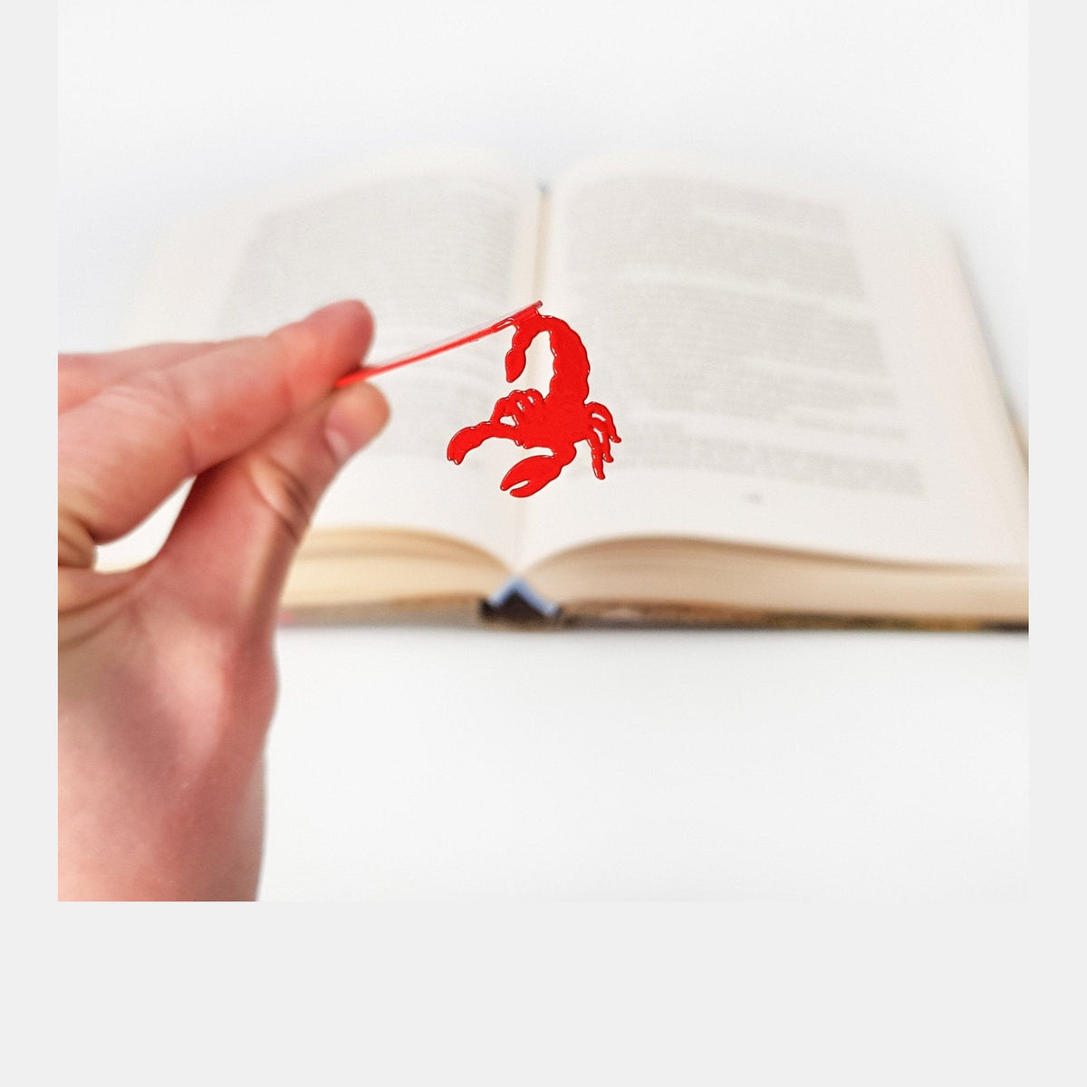 Scorpion metal bookmark in red held in a hand above an open book