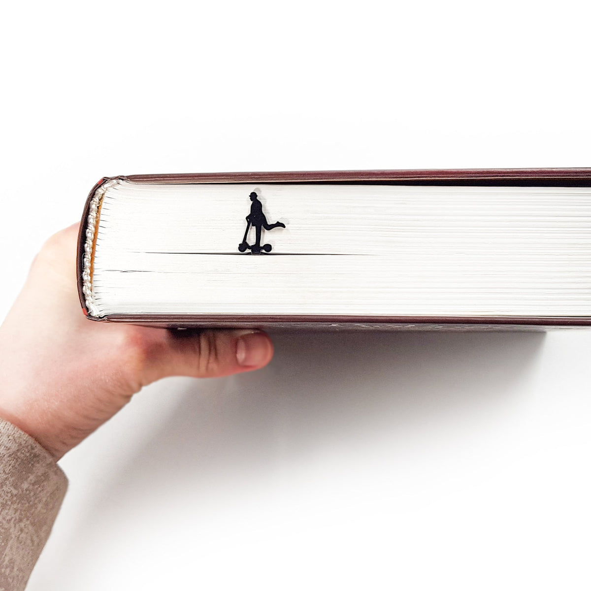 Skater Gentleman metal bookmark held up beside an open book