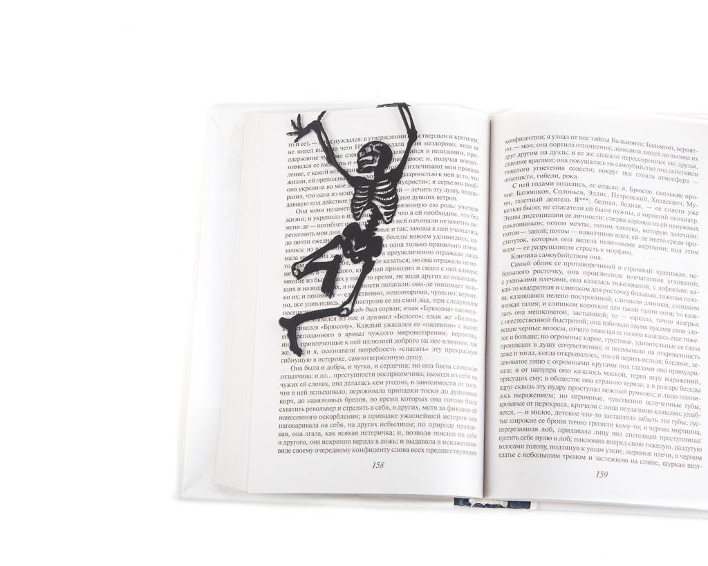 Happy Skeleton metal bookmark resting on the pages of an open book