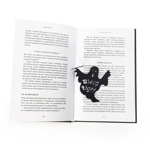 Open book with a black ghost-shaped bookmark inserted between the pages. The ghost features the cut-out phrase “Sleep Tight” 
