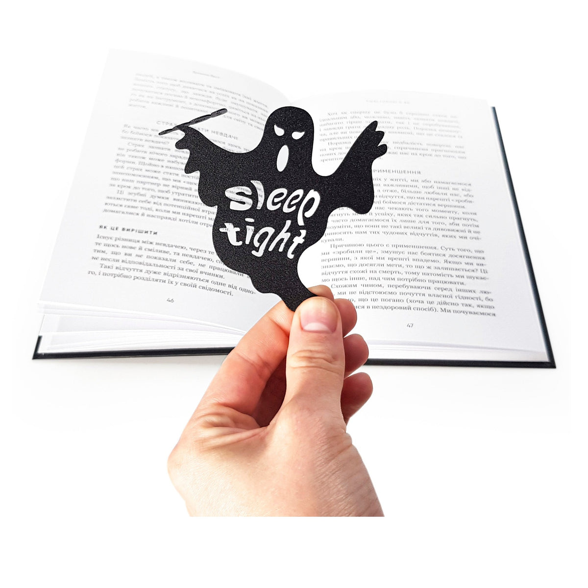 Sleep Tight metal bookmark held in a hand above an open book