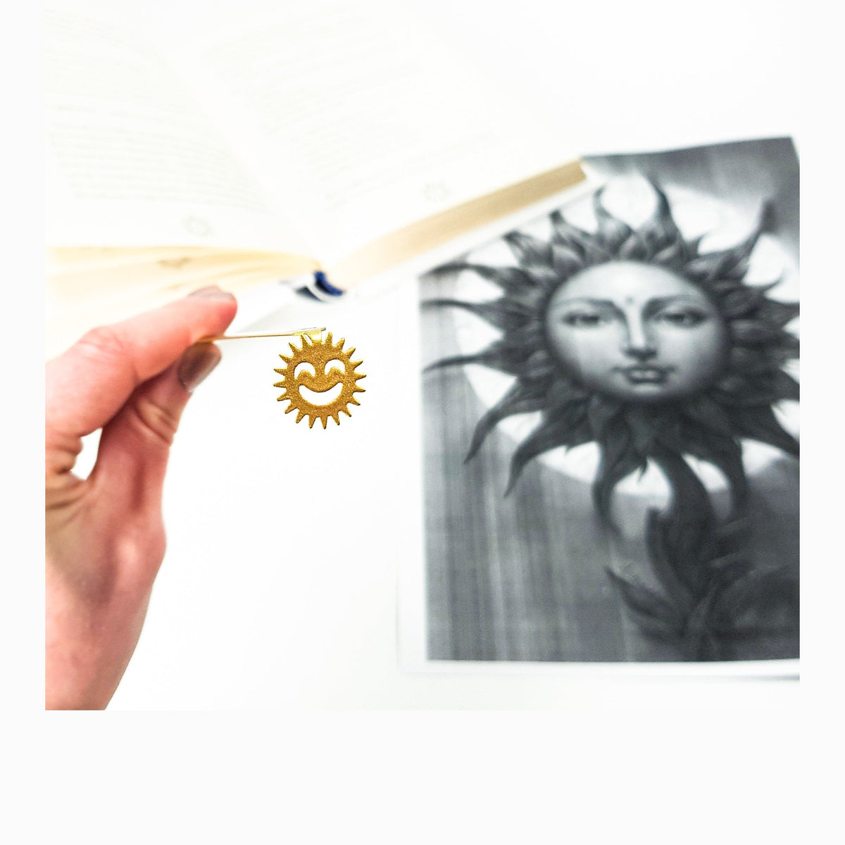 Smiling Sun metal bookmark in gold marking a page in an illustrated book