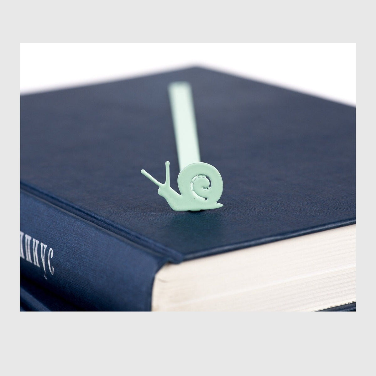 Snail metal bookmark in green in a closed book, only its top showing above the pages
