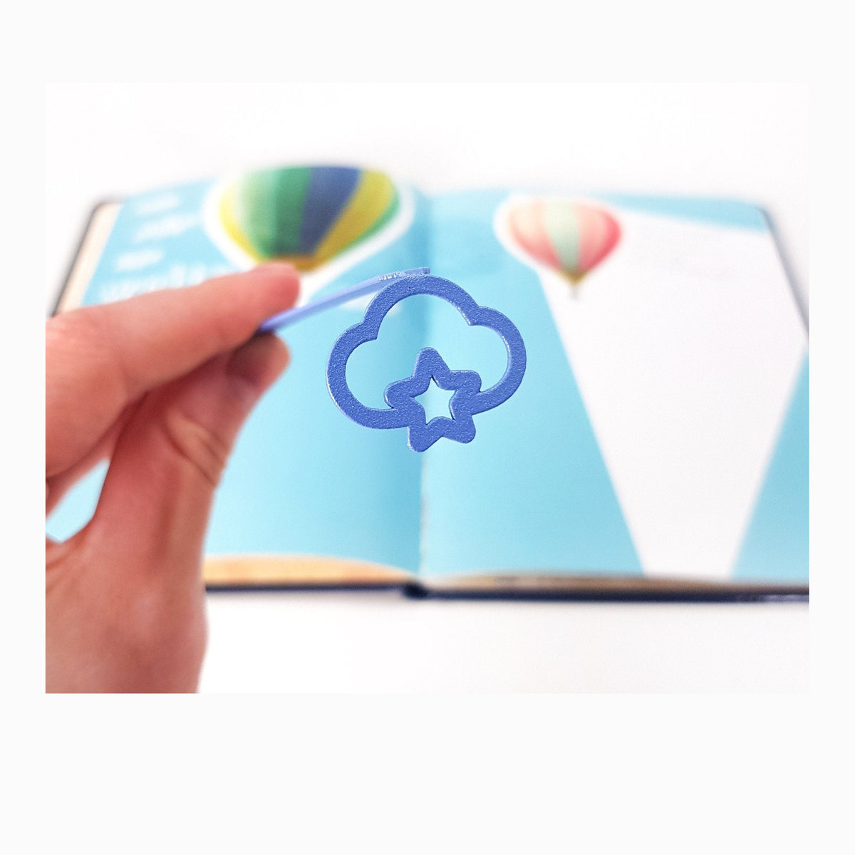 Star Cloud metal bookmark in blue marking a page in an illustrated book