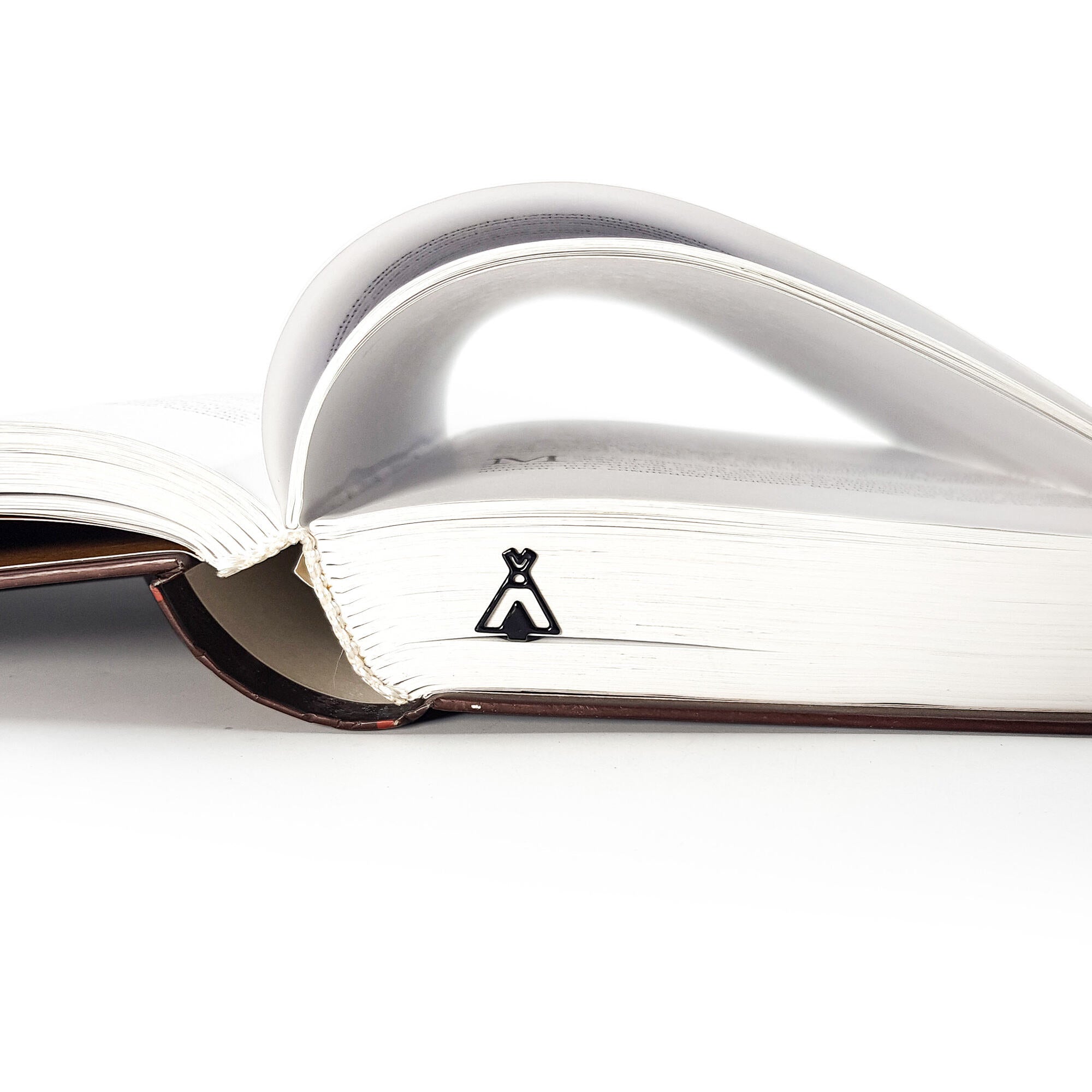 Black teepee-shaped metal bookmark placed in a thick book, with pages gently curved to form an arch above the spine.