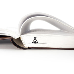 Black teepee-shaped metal bookmark placed in a thick book, with pages gently curved to form an arch above the spine.